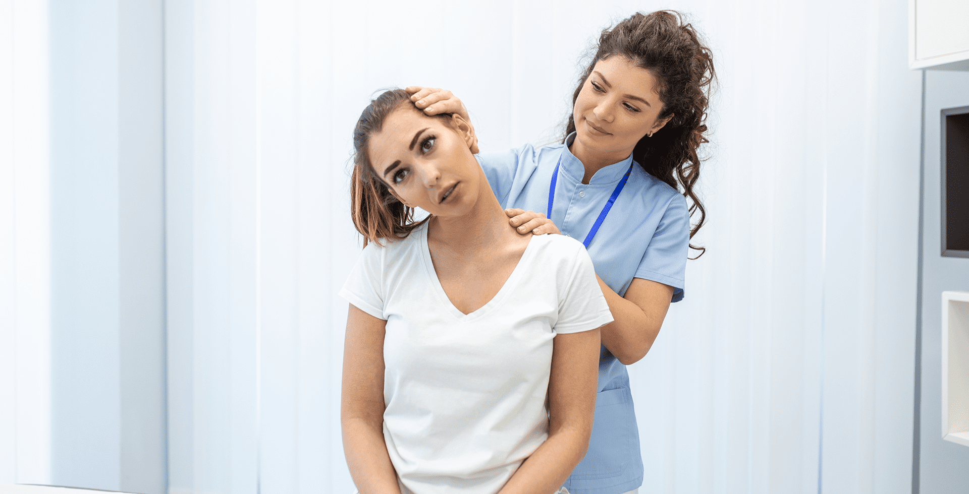 A woman in a white shirt undergoes a neck examination by a healthcare professional in blue scrubs in a clinical setting.